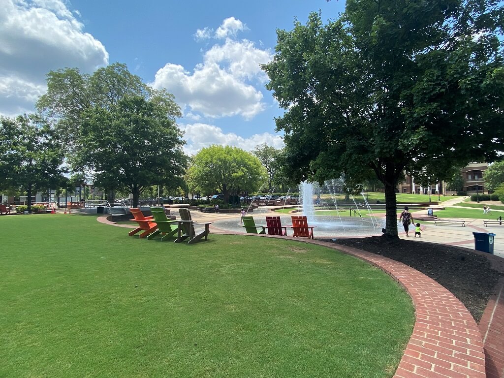 The Duluth town green featuring green grass, lawn chairs, a fountain, and trees