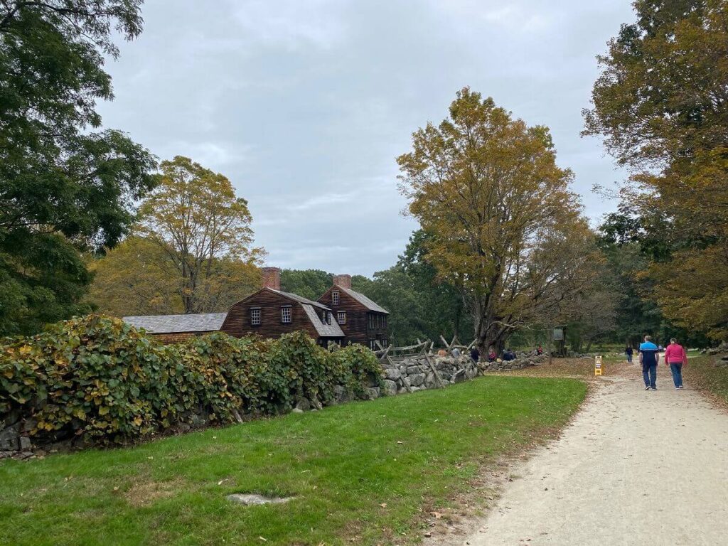 People walk along a gravel path toward a historic inn with yellow and green foliage all around
