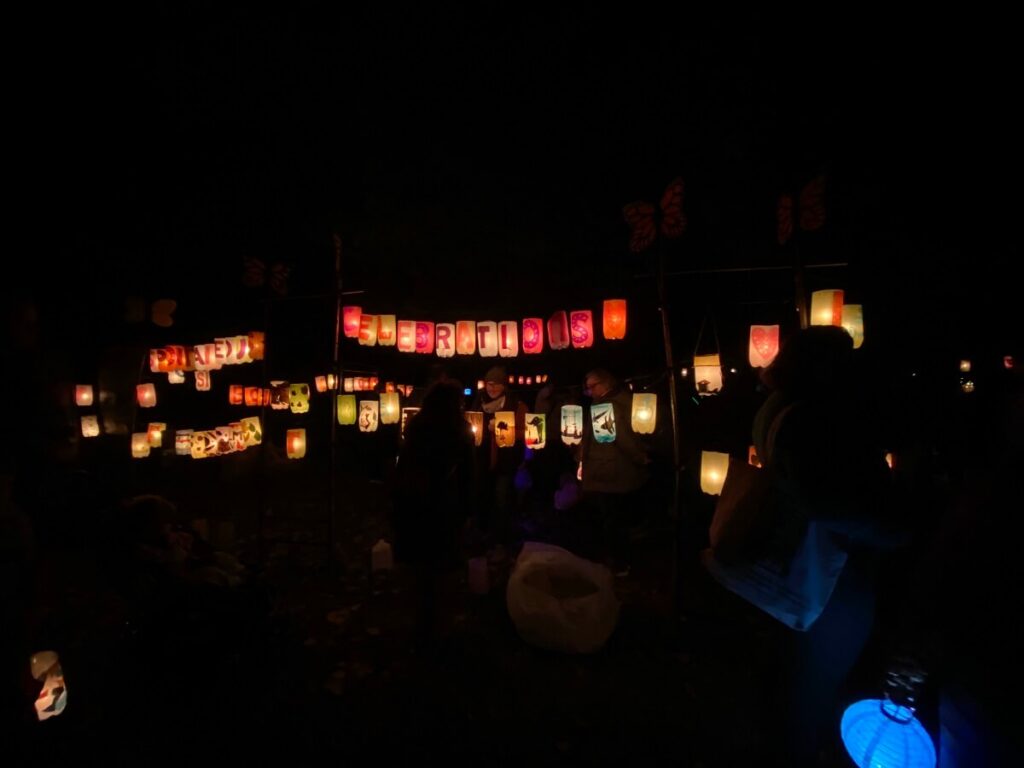 People gather around colorful lanterns hanging from clotheslines and shining in the darkness