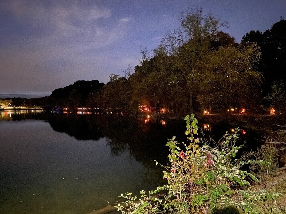 View of Jamaica Pond at night with a long line of lanterns shining among the trees across the water