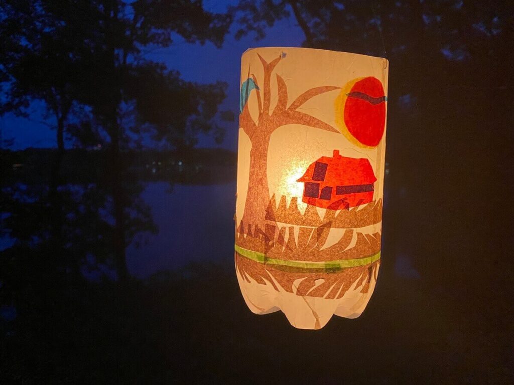 A plastic lantern featuring a red barn and a brown tree with a blue bird on a yellow background