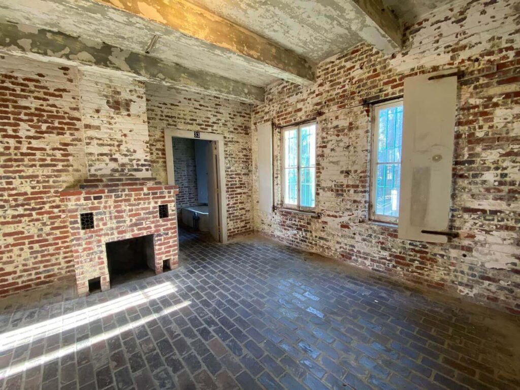 An empty room with a fireplace; the red brick walls have white paint peeling off