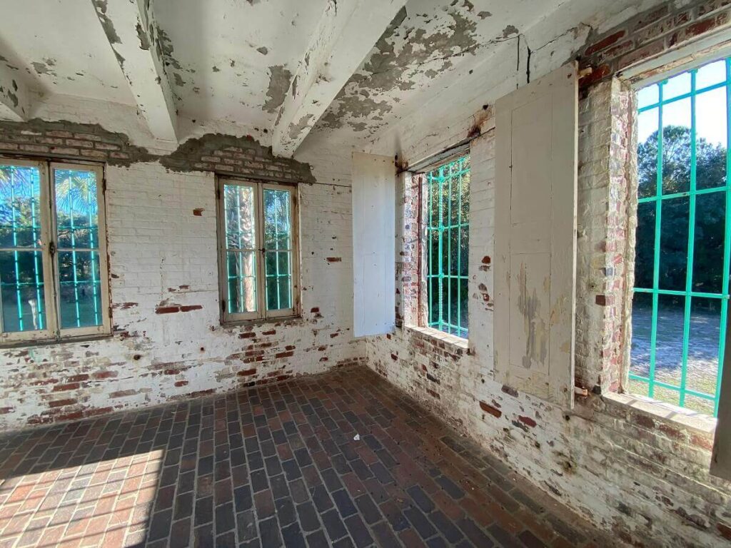 Sun streams through windows into a spacious red brick room with peeling white paint