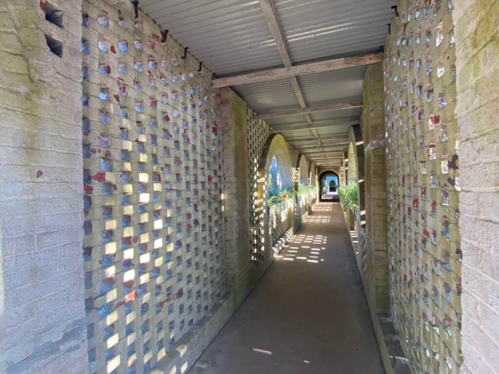 A covered passageway winds between brick walls with plants growing in windows