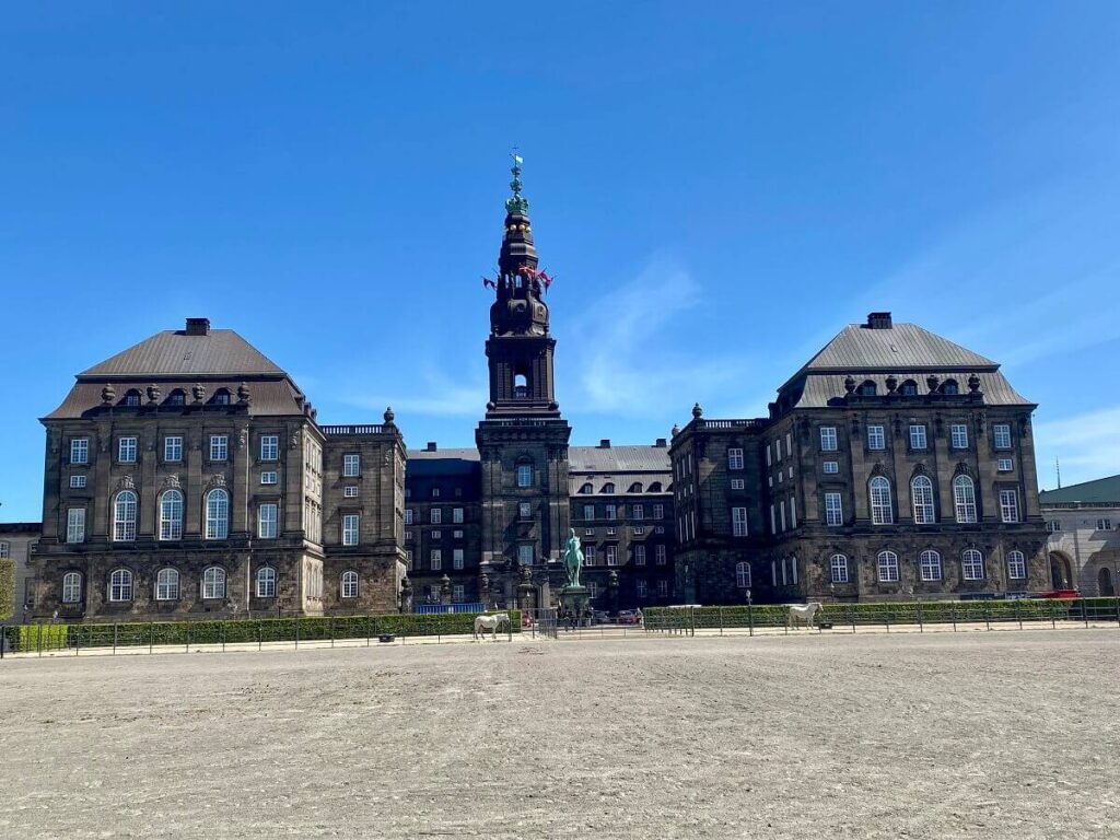 A large castle with two wings and a tower at the center with a parade ground for horses out front