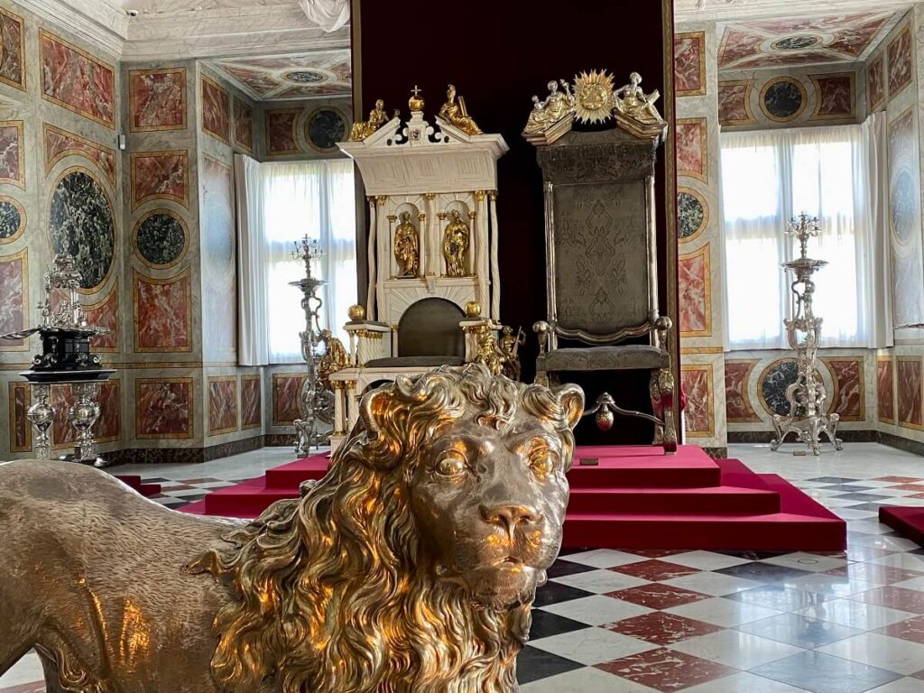 Close up of a life-size silver lion's head with two thrones in the background