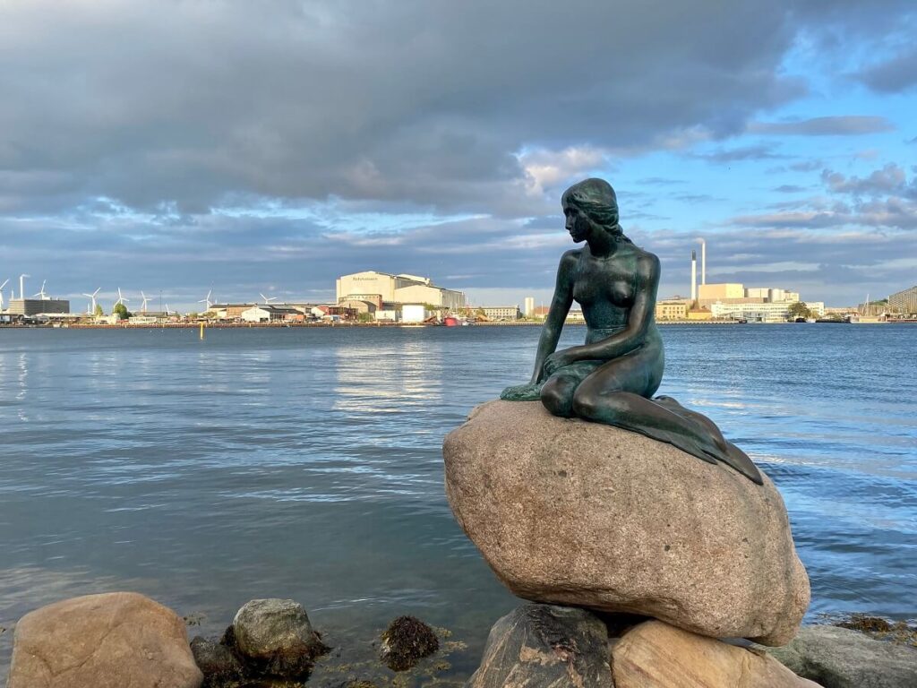 A bronze statue of a mermaid sits on a large rock next to Copenhagen harbor