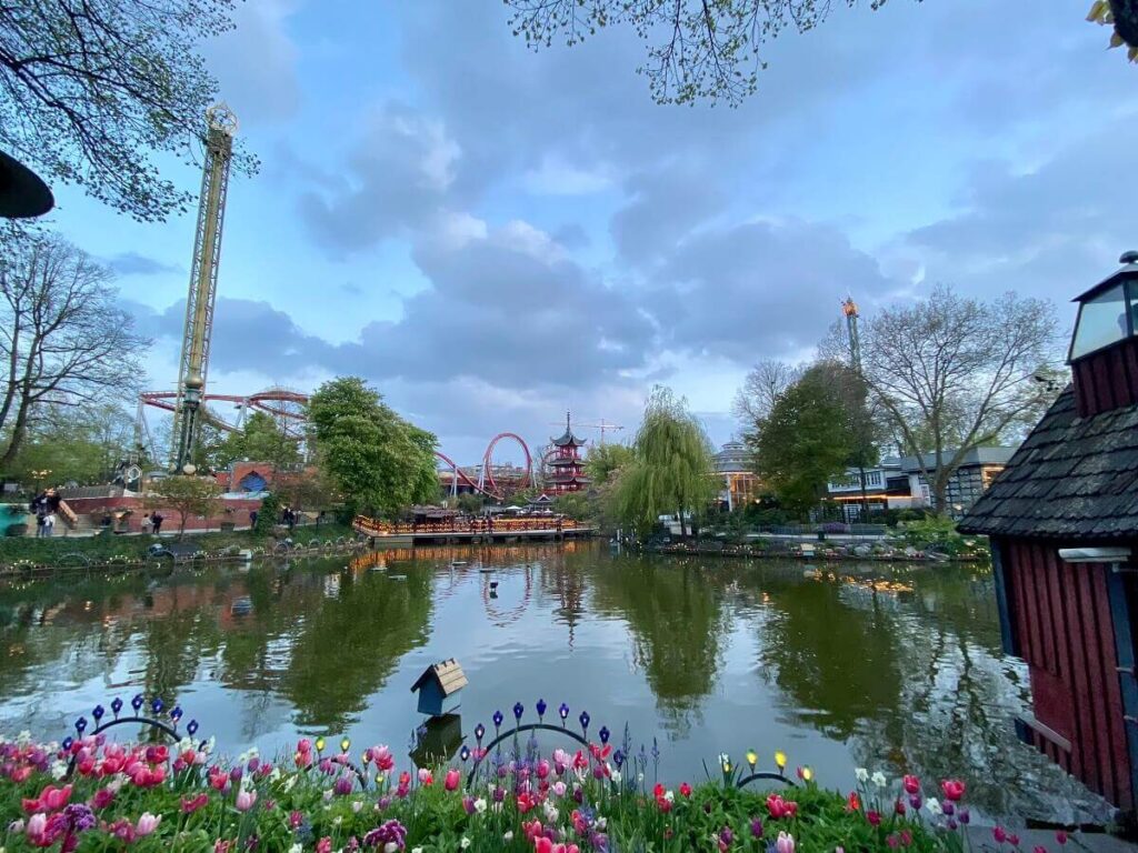 Flowers bloom next to a lake as roller coasters rise in the background in Copenhagen