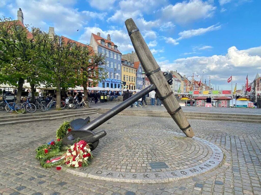 A large anchor with a bouquet of flowers stands in front of the colorful houses of Nyhavn